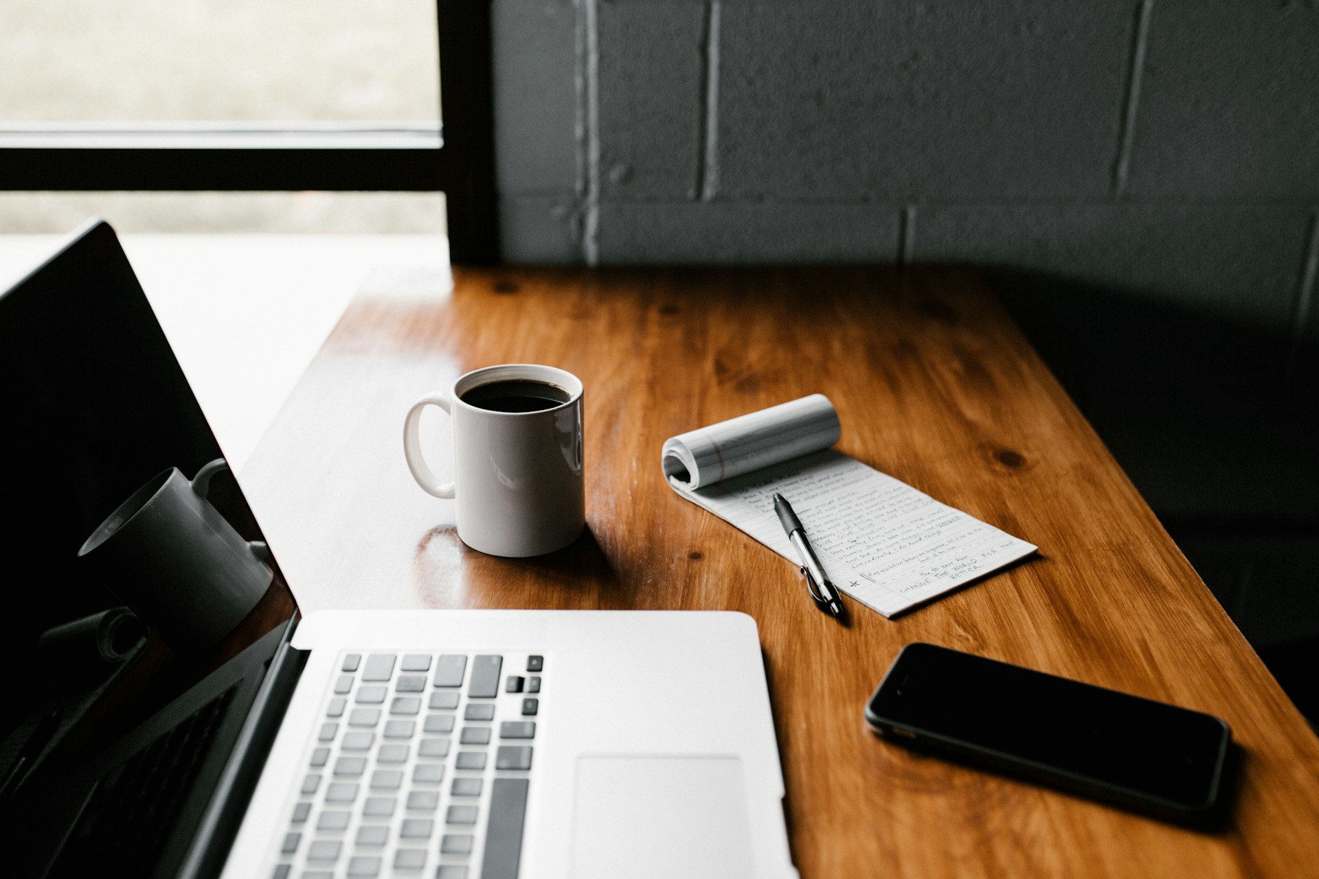 A computer, coffee, and notepad on a desk